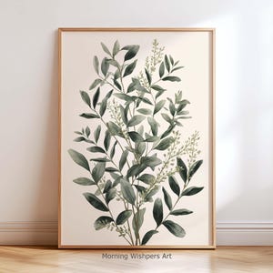 May include: A framed vertical wall art print featuring a watercolor illustration of dark green eucalyptus leaves and delicate sprigs on a cream background. The text Morning Wishpers Art is printed in small black letters at the bottom center.
