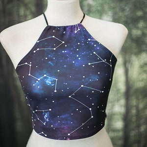 Könnte beinhalten: Ein Halstuch-Top mit dunkelblauem Hintergrund und einem weißen Sternenbild-Druck. Das Oberteil ist aus dehnbarem Stoff und hat eine lockere Passform.