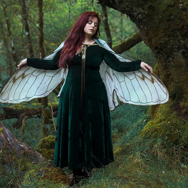 A woman in the woods, wearing a long green velvet dress with fake wings over her shoulders.