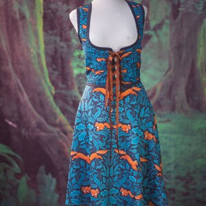May include: A blue and orange dress with a floral pattern and brown ribbon lacing. The dress is on a mannequin against a green and brown background.