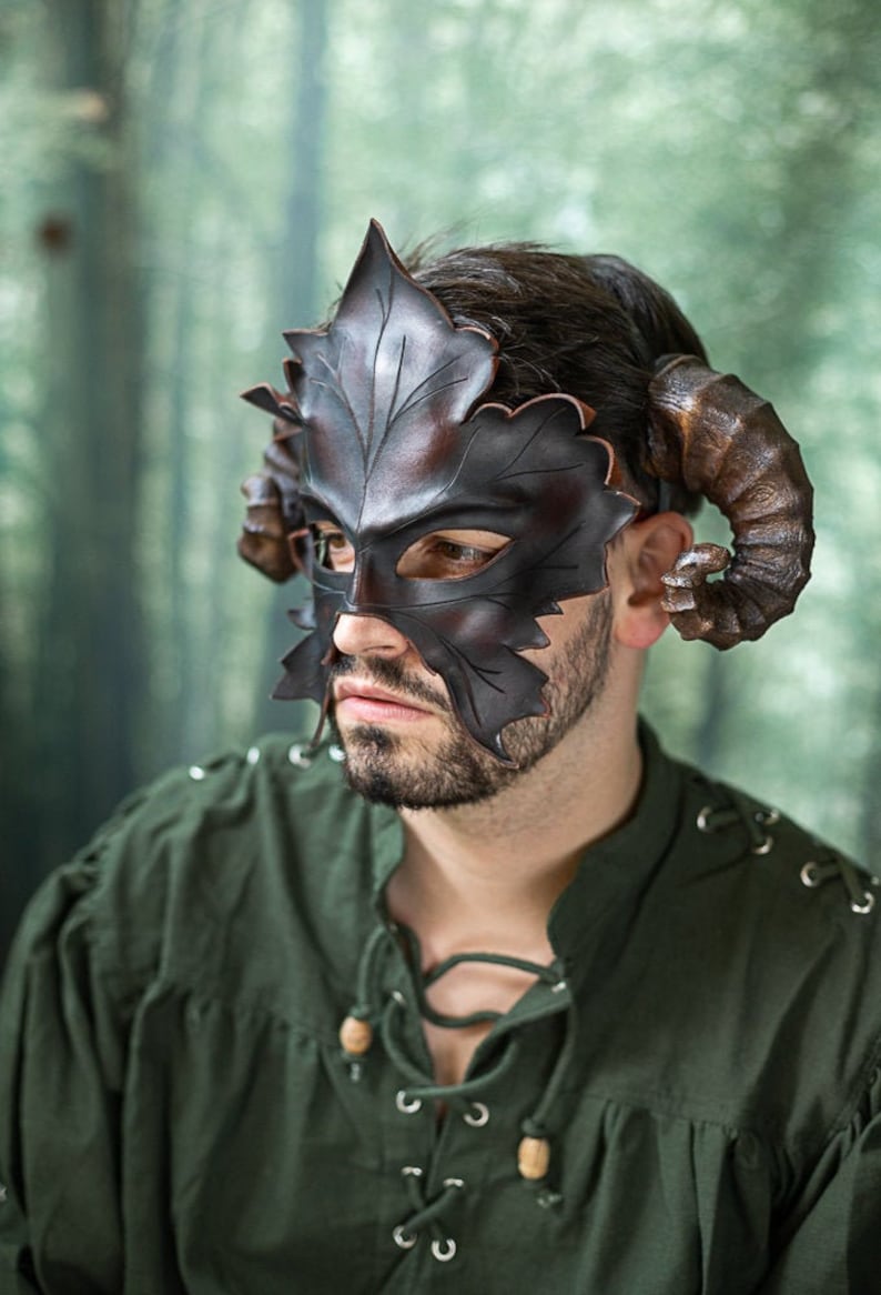 Puede incluir: Una m&aacute;scara de cuero marr&oacute;n con un dise&ntilde;o de hoja y cuernos. La m&aacute;scara cubre los ojos y parte de la nariz y la frente. La m&aacute;scara la lleva una persona con barba.