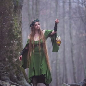 May include: A woman wearing a green dress and a leafy crown holds a stained glass lantern in a woodland setting.