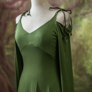 May include: A green sleeveless dress with long sleeves that are tied at the shoulders. The dress has a V-neckline and a flowing skirt.