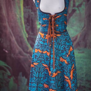 May include: A blue and orange dress with a forest print and a brown lace-up bodice. The dress is on a mannequin against a green and brown background.