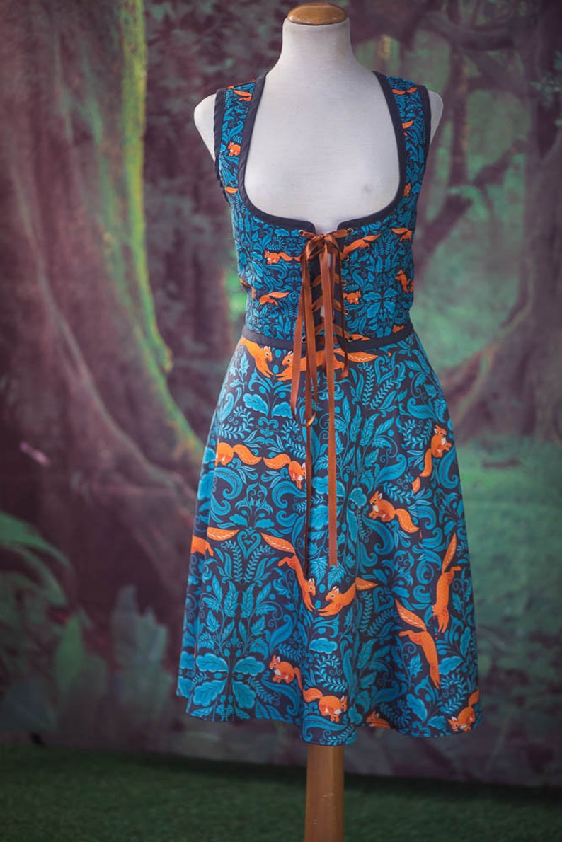 May include: A blue and orange dress with a forest print and a brown lace-up bodice. The dress is on a mannequin against a green and brown background.