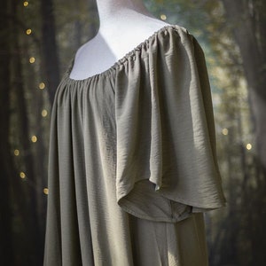 K&ouml;nnte beinhalten: Ein locker sitzendes, olivgr&uuml;nes, schulterfreies Kleid mit kurzen, gekr&auml;uselten &Auml;rmeln. Das Kleid ist aus einem weichen, flie&szlig;enden Stoff gefertigt.