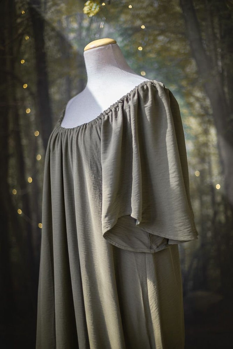 K&ouml;nnte beinhalten: Ein locker sitzendes, olivgr&uuml;nes, schulterfreies Kleid mit kurzen, gekr&auml;uselten &Auml;rmeln. Das Kleid ist aus einem weichen, flie&szlig;enden Stoff gefertigt.