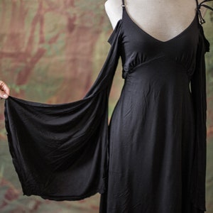 May include: A black maxi dress with long sleeves and a V-neckline. The sleeves are cut out at the shoulders and have a flowing, draped look.
