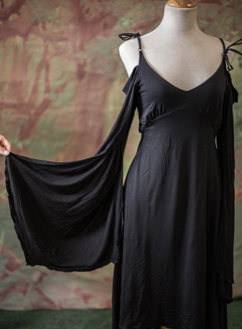 May include: A black maxi dress with long sleeves and a V-neckline. The sleeves are cut out at the shoulders and have a flowing, draped look.
