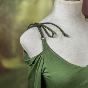 May include: A green off-the-shoulder dress with long sleeves and a tied strap detail.