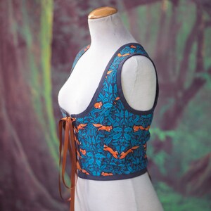 May include: A blue and orange patterned corset with brown lacing. The corset is on a white dress form against a green and purple background.