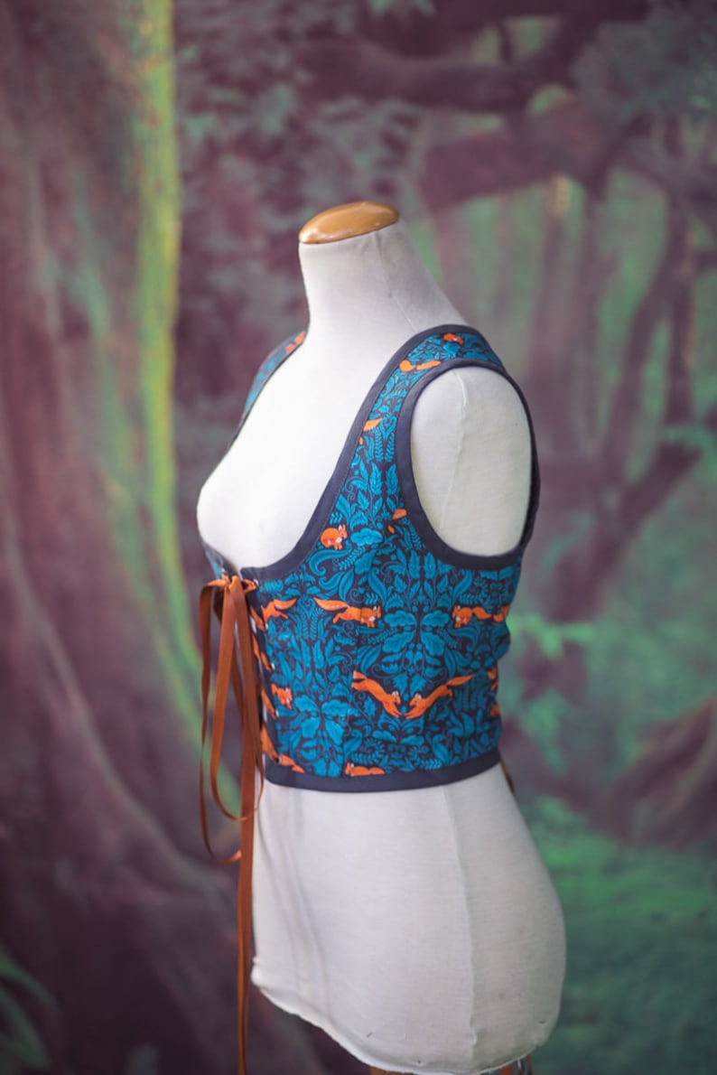 May include: A blue and orange patterned corset with brown lacing. The corset is on a white dress form against a green and purple background.