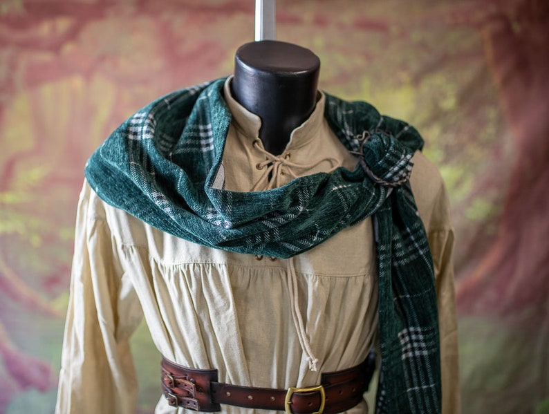 May include: A cream-colored shirt with a green and white plaid scarf. The shirt has a lace-up neckline and a brown leather belt.
