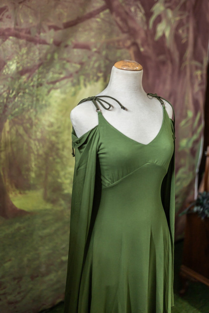 May include: A green, sleeveless dress with a V-neckline and a flowing skirt. The dress has a tie at the shoulder and is on a white mannequin.