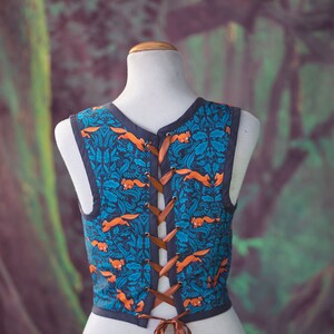 May include: A sleeveless vest with a blue and orange pattern of foxes and leaves. The vest has a brown lace-up back.