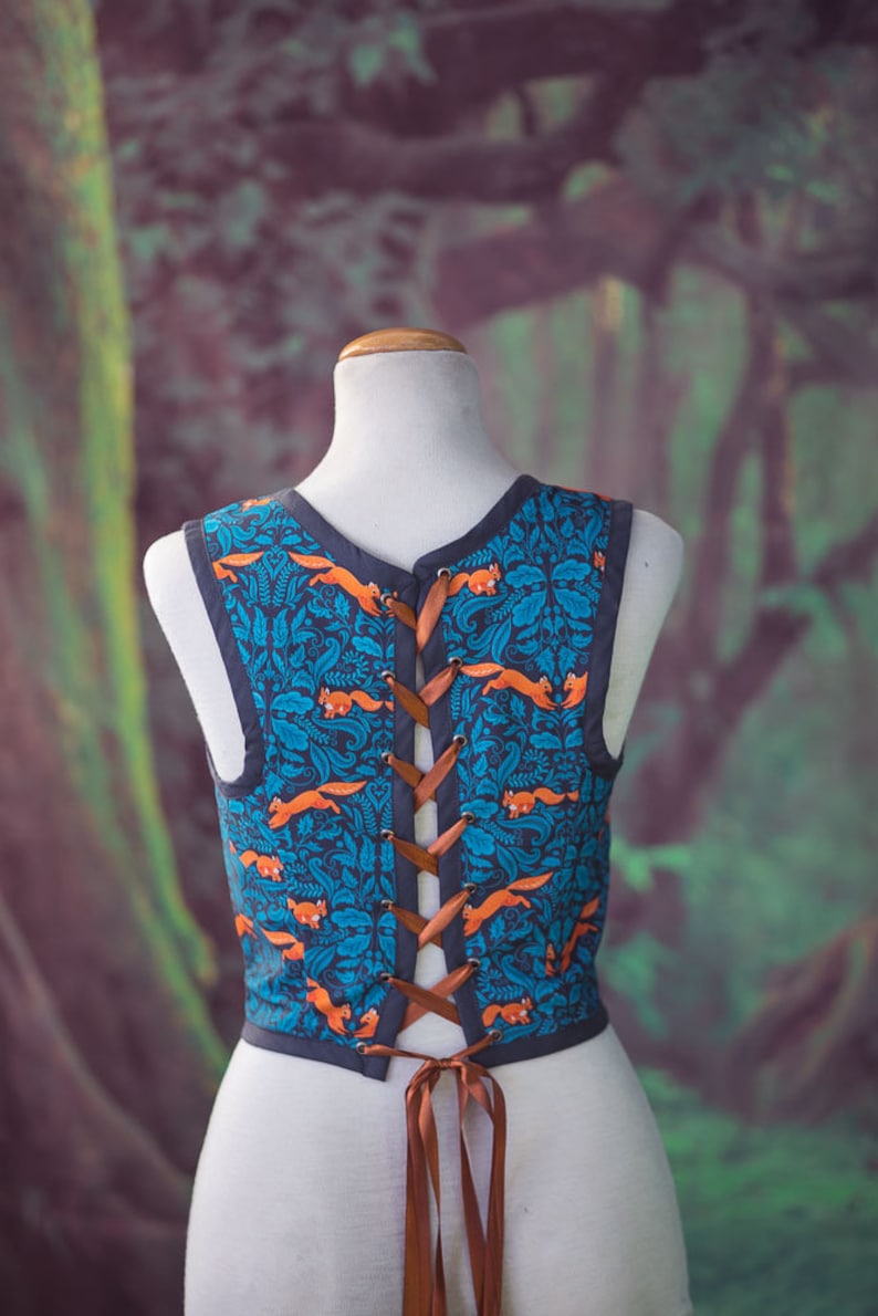 May include: A sleeveless vest with a blue and orange pattern of foxes and leaves. The vest has a brown lace-up back.