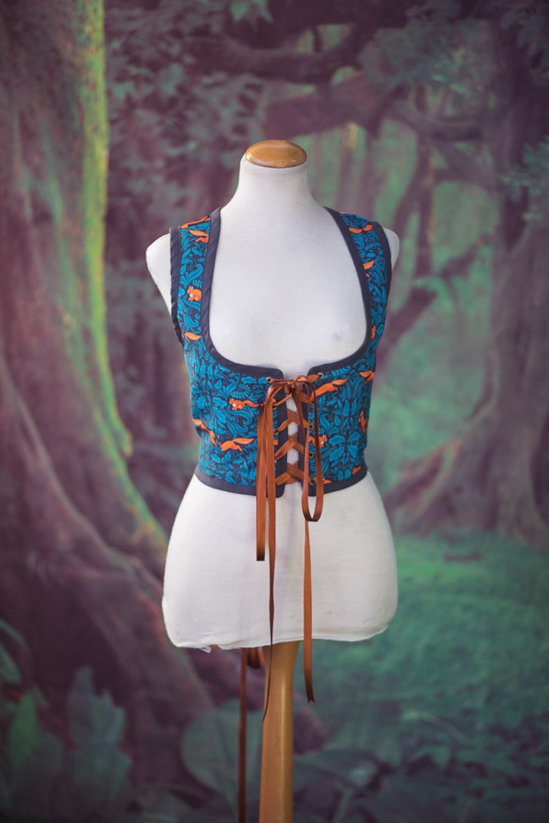 May include: A blue and orange patterned corset with brown laces. The corset is on a white mannequin.