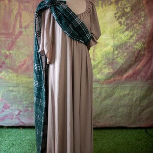 May include: A beige maxi dress with a green and white plaid scarf draped over the shoulder. The scarf is tied in a knot at the neck.