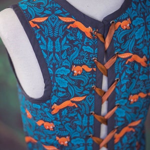 May include: A sleeveless vest with a blue and teal floral pattern featuring orange squirrels. The vest has a brown ribbon lacing up the back.