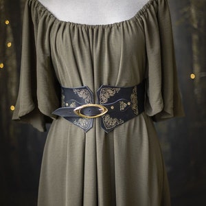 K&ouml;nnte beinhalten: Ein gr&uuml;nes, schulterfreies Kleid mit einem breiten schwarzen Lederg&uuml;rtel mit einer goldenen Schnalle und filigranen Blumenmustern.
