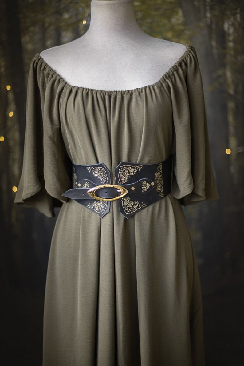 K&ouml;nnte beinhalten: Ein gr&uuml;nes, schulterfreies Kleid mit einem breiten schwarzen Lederg&uuml;rtel mit einer goldenen Schnalle und filigranen Blumenmustern.