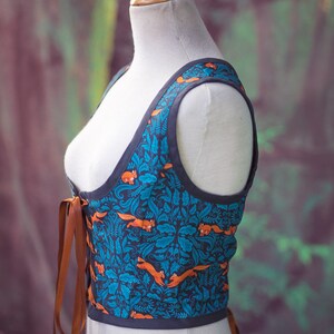 May include: A blue and orange patterned corset with brown lacing. The corset is sleeveless and has a fitted bodice.