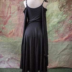 May include: A black off-the-shoulder dress with long sleeves and a flowing skirt. The dress is on a mannequin against a painted backdrop.