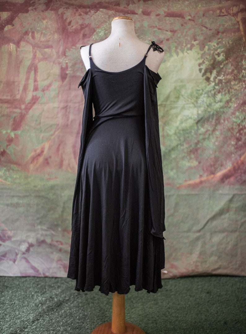 May include: A black off-the-shoulder dress with long sleeves and a flowing skirt. The dress is on a mannequin against a painted backdrop.