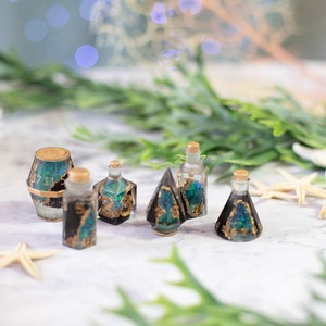 May include: A set of six black and gold dice with green glitter accents. The dice are shaped like a barrel, a bottle, a pyramid, and a cone. The dice are on a white surface.
