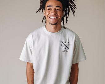 May include: A cream-coloured t-shirt with a black graphic design on the upper left chest. The design features crossed lines with the letters "A", "P", and "P" and the text "Milo since 2024". The shirt has short sleeves and a crew neck.