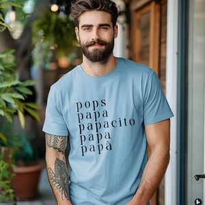 Pode incluir: Camiseta azul clara com as palavras "pops, papa, papacito, papa, papà" impressas em preto. A camiseta é feita de um material macio e é adequada para uso casual. Um ótimo presente para um pai ou avô.