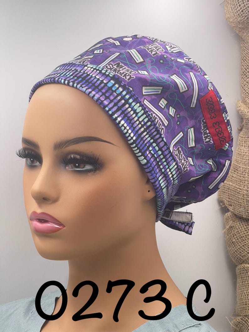 Puede incluir: Un gorro quir&uacute;rgico morado con un patr&oacute;n repetido de gr&aacute;ficos de tem&aacute;tica m&eacute;dica y las palabras "NEURO SURGERY". El gorro tiene un borde contrastante y un parche rojo con texto. El n&uacute;mero "0273C" est&aacute; impreso en la parte inferior.
