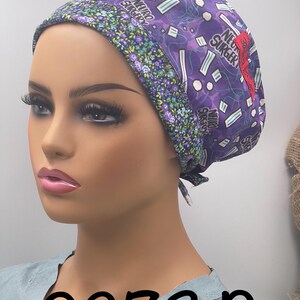 Puede incluir: Un gorro quir&uacute;rgico morado con las palabras "Neuro Surgeon" y gr&aacute;ficos de tem&aacute;tica m&eacute;dica. El gorro tiene un borde con estampado floral y un acento rojo. El n&uacute;mero "0273D" est&aacute; impreso en negro en la parte inferior.