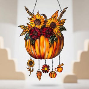 Puede incluir: Decoración de calabaza de vidriera llena de girasoles y flores rojas. La calabaza es naranja con un tallo y cuelga de una cadena. Los dijes adicionales incluyen un girasol, una hoja, una flor, una calabaza y una taza.