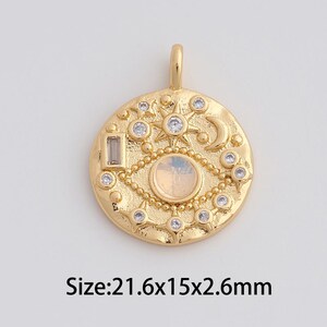 May include: Gold-colored pendant with an eye design, featuring a central iridescent stone and surrounding clear crystals. The pendant is round, with a loop at the top for attachment. Dimensions are 21.6mm x 15mm x 2.6mm.