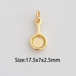 Puede incluir: Colgante dorado con forma de sartén pequeña. Tiene un lazo en la parte superior para sujetar a una cadena y una base circular. Tamaño: 17,5x7x2,5 mm.