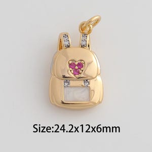 May include: Gold-colored backpack charm with a red heart-shaped gem and clear crystals. The charm measures approximately 0.95 x 0.47 x 0.24 inches. The charm has a small loop at the top for attaching to a necklace or bracelet.