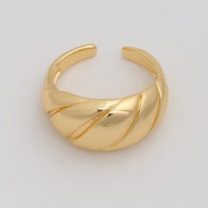 Puede incluir: Un anillo dorado con un diseño texturizado y acanalado. El anillo tiene un diseño abierto, lo que permite un ajuste ajustable. El anillo de metal brillante se encuentra sobre un fondo blanco.