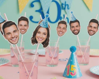 May include: A birthday party setting with personalized face cutouts on straws in glasses of pink liquid. A blue party hat with the number 15 and a banner that says "30th" are also visible. The table is set with plates and decorations.