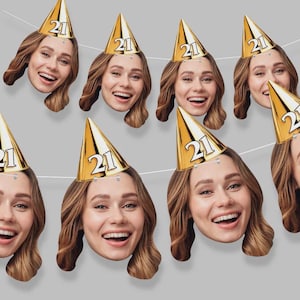 May include: A celebratory banner with multiple smiling faces, each wearing a gold party hat with the number "21". The faces are strung together, forming a garland. The background is a plain, neutral grey.