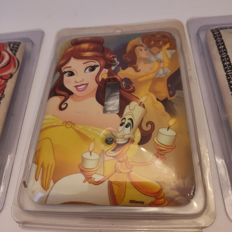 Pu&ograve; includere: Una copertura decorativa per interruttore della luce con un'illustrazione colorata di Belle, la Bestia e Lumi&egrave;re de La Bella e la Bestia di Disney. La copertura &egrave; gialla e ha una finitura lucida. Il logo Disney &egrave; visibile.