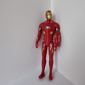Op de afbeelding: Een rood en goud Iron Man actiefiguur. De figuur heeft een gouden helm en accenten, met een blauw borststuk. De figuur staat in een hoek tegen een witte achtergrond.