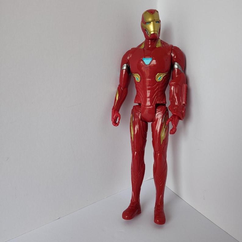 Op de afbeelding: Een rode Iron Man actiefiguur met gouden en zilveren accenten. De figuur heeft een gouden helm en een blauw borststuk. De figuur staat in een hoek tegen een witte achtergrond.