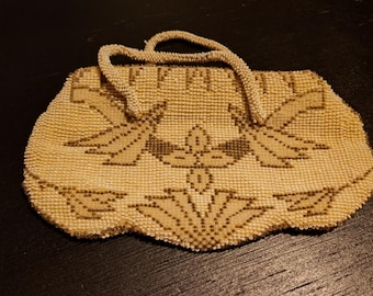 May include: Cream-colored beaded handbag with a handle. The bag features a floral design in shades of brown. The beaded purse has a scalloped edge and a structured shape, suggesting a vintage or antique style.