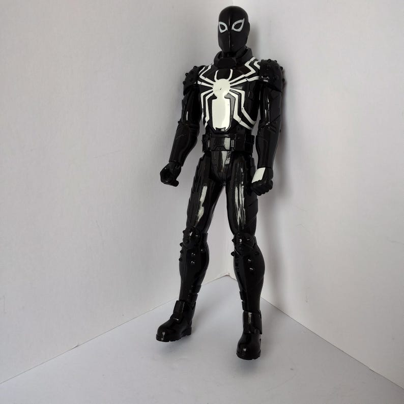 Op de afbeelding: Een zwart actiefiguur van een superheld met een wit spinnenembleem op de borst. Het figuur heeft een zwart masker en het pak is gedetailleerd met witte accenten. Het figuur staat in een neutrale pose.