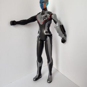 Op de afbeelding: Gedetailleerd actiefiguur van een personage met blauwe huid, oranje en blauwe markeringen en een zwart en zilver pak. Het figuur heeft een dynamische pose met &eacute;&eacute;n arm uitgestrekt. Het pak heeft het Avengers-logo.