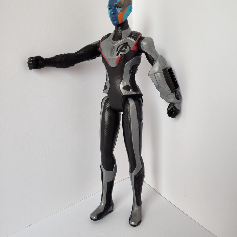 Op de afbeelding: Gedetailleerd actiefiguur van een personage met blauwe huid, oranje en blauwe markeringen en een zwart en zilver pak. Het figuur heeft een dynamische pose met &eacute;&eacute;n arm uitgestrekt. Het pak heeft het Avengers-logo.