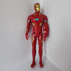 Op de afbeelding: Een rood en goud Iron Man actiefiguur. Het figuur heeft een rode body met gouden accenten op de armen, benen en borst. De helm is goudkleurig en de borst heeft een blauw licht. Het figuur staat rechtop.