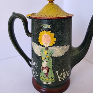 May include: A decorative, hand-painted coffee pot with a dark green body and a yellow lid. The pot features a painted angel design with the words "Be ye kind". The handle and spout are dark green.