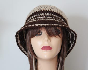 May include: A crocheted bucket hat in shades of brown and beige. The hat features a striped pattern around the crown and brim. The hat is displayed on a mannequin head with brown hair and a neutral background.